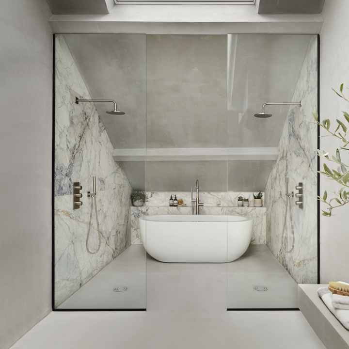 Lifestyle image of a Hotel style bathroom, featuring glass shower screens separating a wet room areas with twin wall mounted showers and a freestanding bathtub